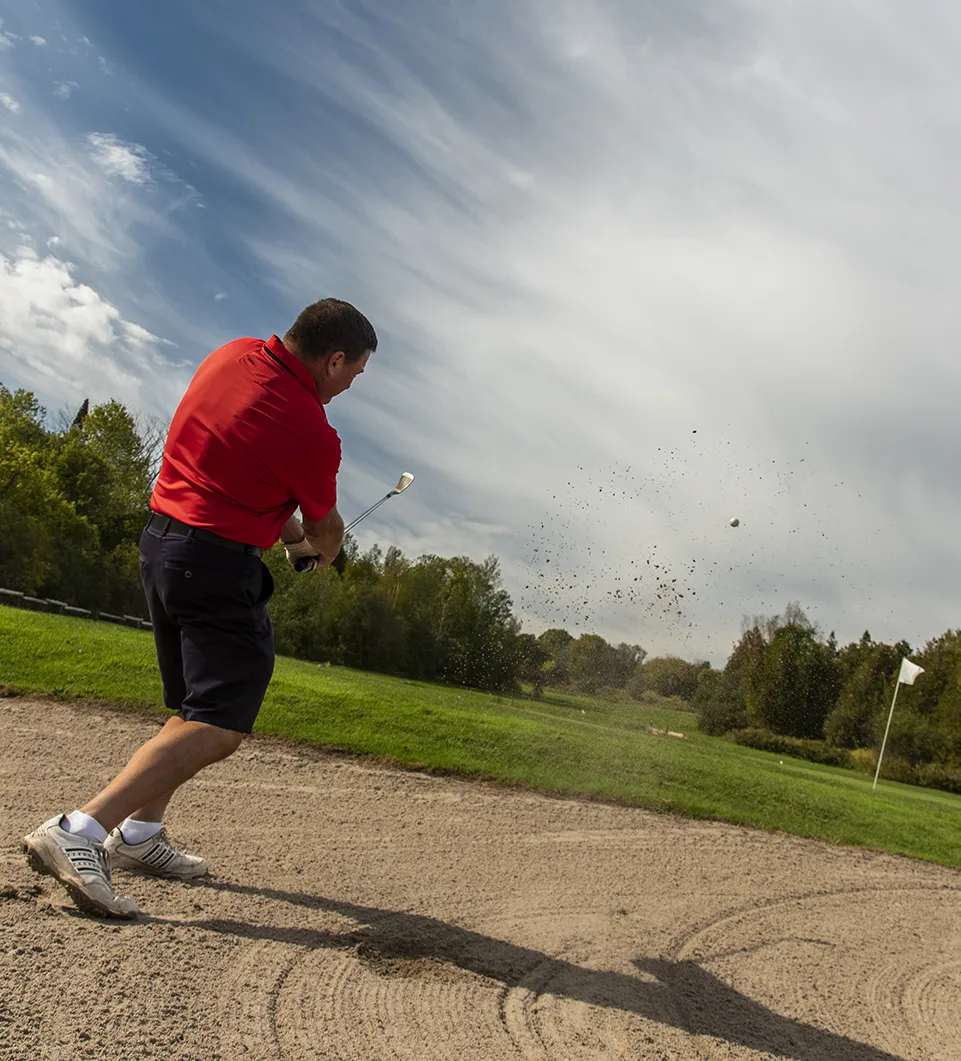 Man golfing out of a bunker onto a green